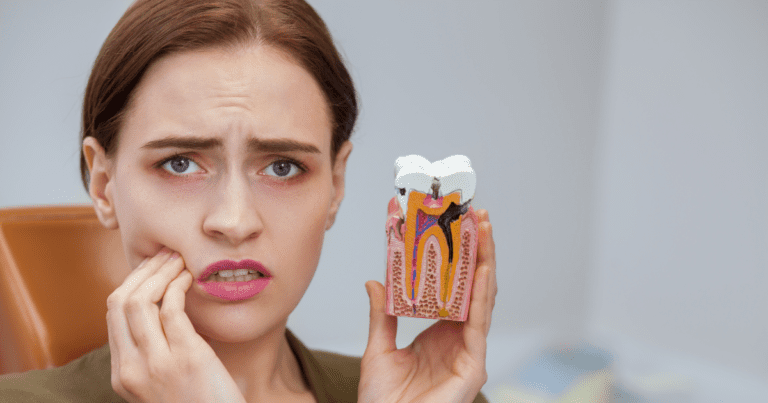Woman experiencing tooth pain while holding a model of a tooth with decay